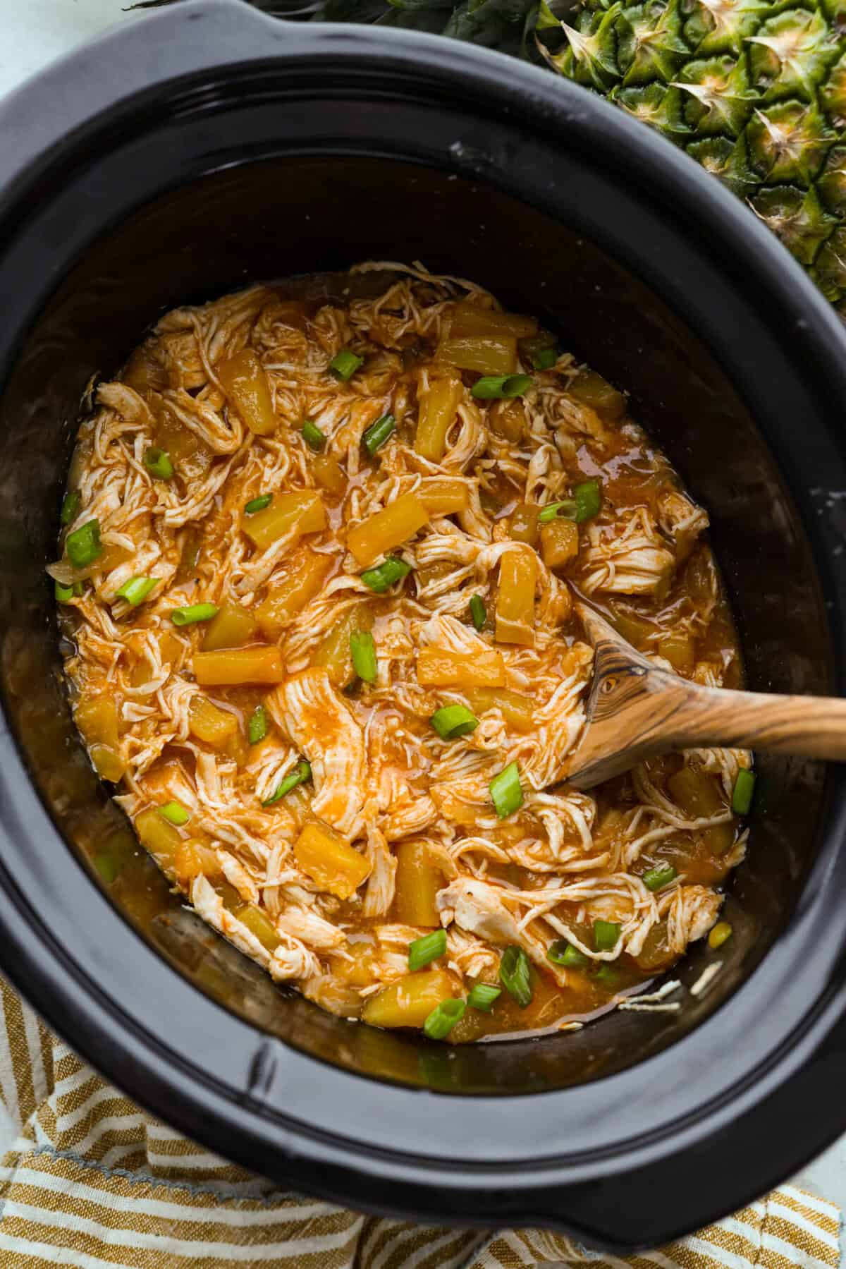Slow cooker Aloha chicken is sweet, smoky, and so easy to throw together! Tender chicken cooks with pineapple, onion, and barbecue sauce until it’s full of flavor and ready to shred. Serve it over rice for a simple dinner the whole family will love. Crockpot full of tender slow cooker aloha chicken with pineapple and green onions.