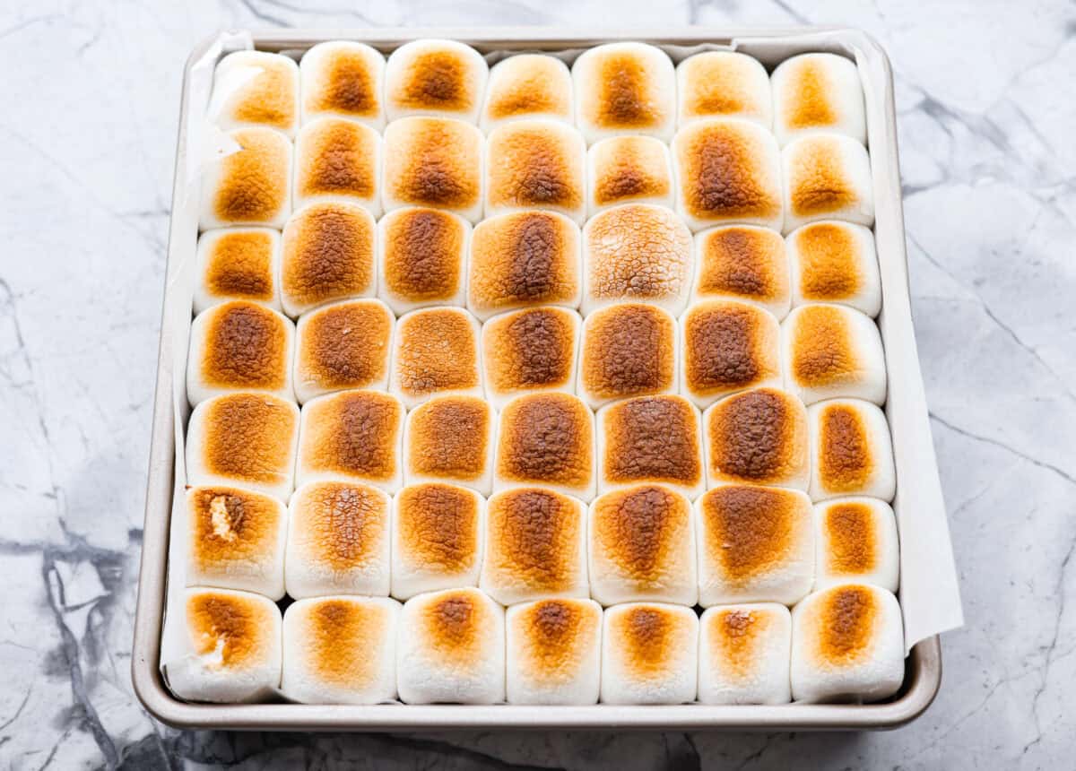 These s'mores brownies bring all the nostalgia of a campfire treat straight to your kitchen. Layers of buttery graham crackers, melty chocolate, fudgy brownie, and gooey marshmallows make every bite taste like summer. No fire pit required! Top down shot of the toasted marshmallows on the S'more Brownies.