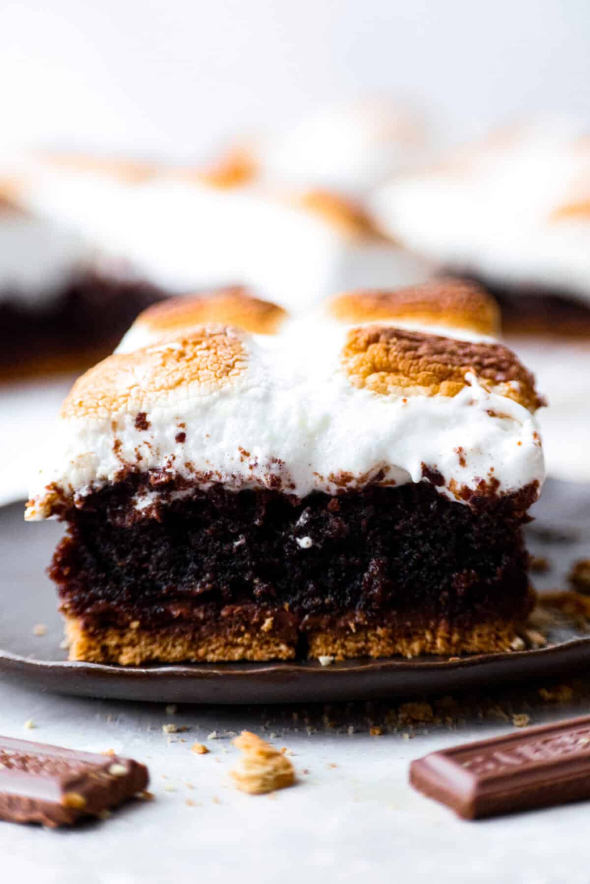 These s'mores brownies bring all the nostalgia of a campfire treat straight to your kitchen. Layers of buttery graham crackers, melty chocolate, fudgy brownie, and gooey marshmallows make every bite taste like summer. No fire pit required! Close up shot of the side of a S'mores brownie.