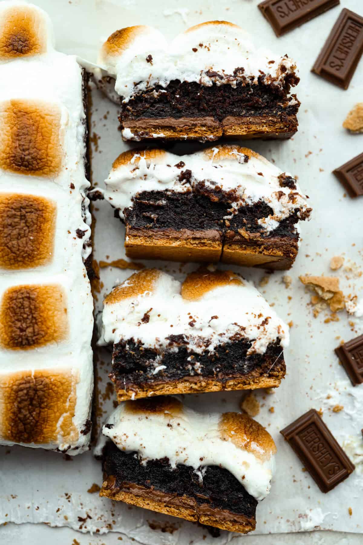 These s'mores brownies bring all the nostalgia of a campfire treat straight to your kitchen. Layers of buttery graham crackers, melty chocolate, fudgy brownie, and gooey marshmallows make every bite taste like summer. No fire pit required! Overhead shot of slices of S'mores brownies on their side so you can see all of the gooey layers.