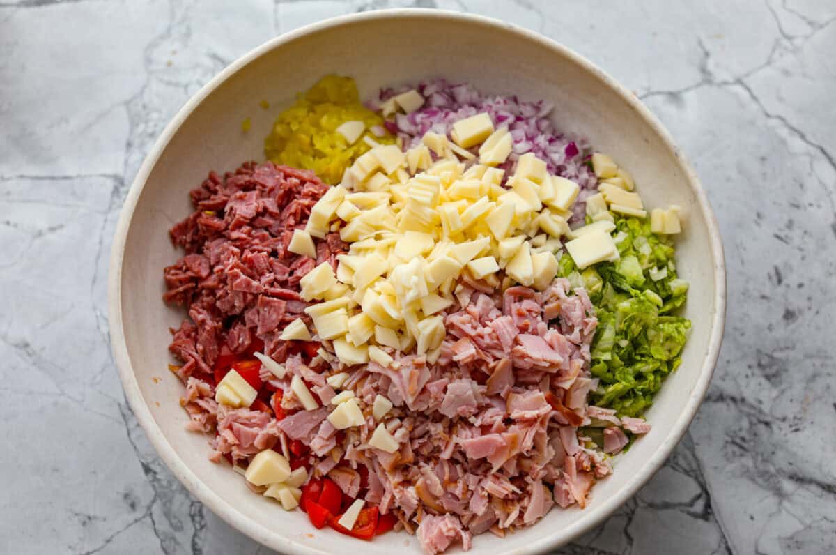 If you're a fan of deli sandwiches, you will love this sub in a tub dip! Made with deli meats, cheese, crisp veggies, and a creamy tangy dressing, it tastes just like your favorite sandwich shop sub in dip form! Bowl of chopped up ingredients.