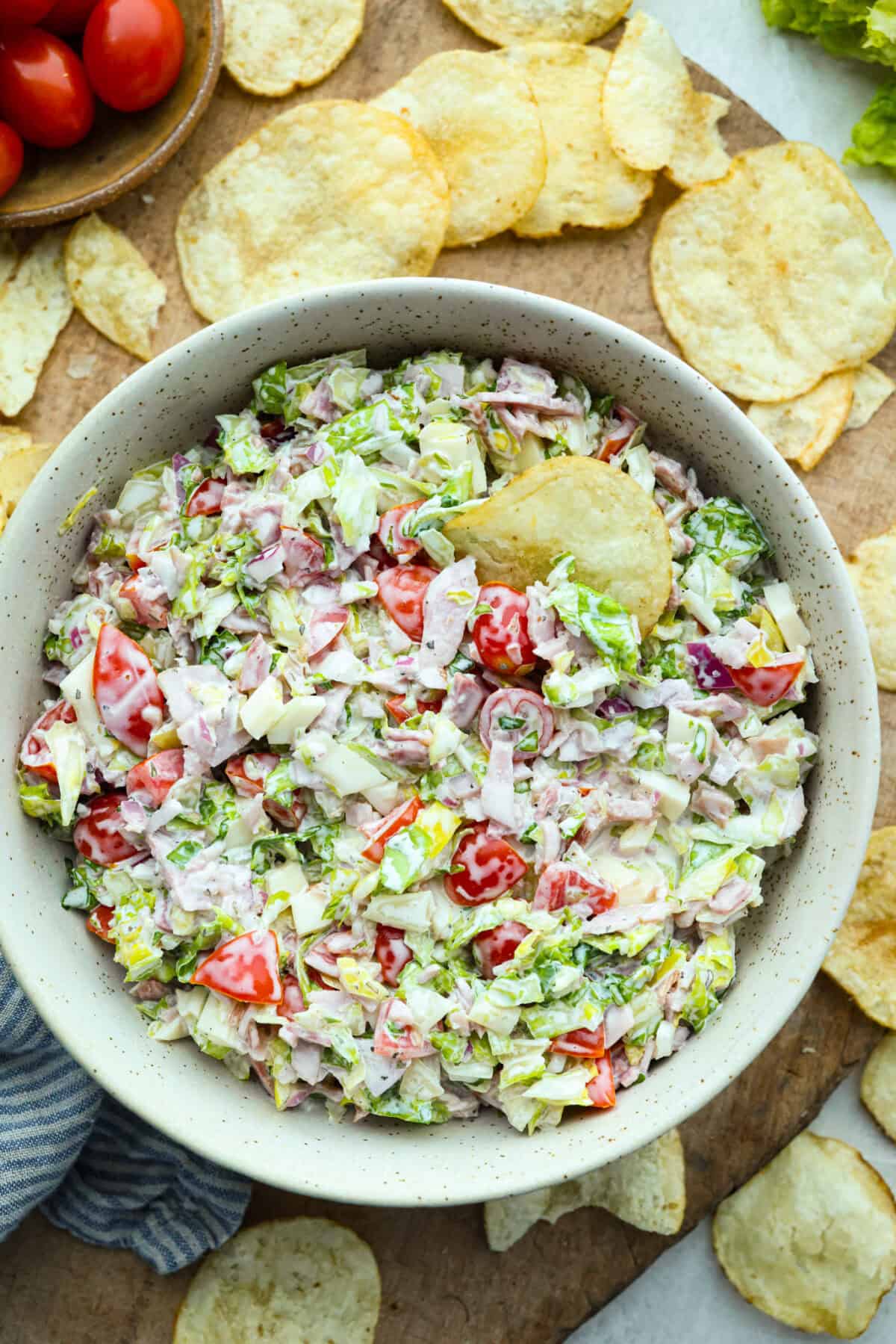 If you're a fan of deli sandwiches, you will love this sub in a tub dip! Made with deli meats, cheese, crisp veggies, and a creamy tangy dressing, it tastes just like your favorite sandwich shop sub in dip form! Bowl of sub in a tub dip, surrounded by potato chips.