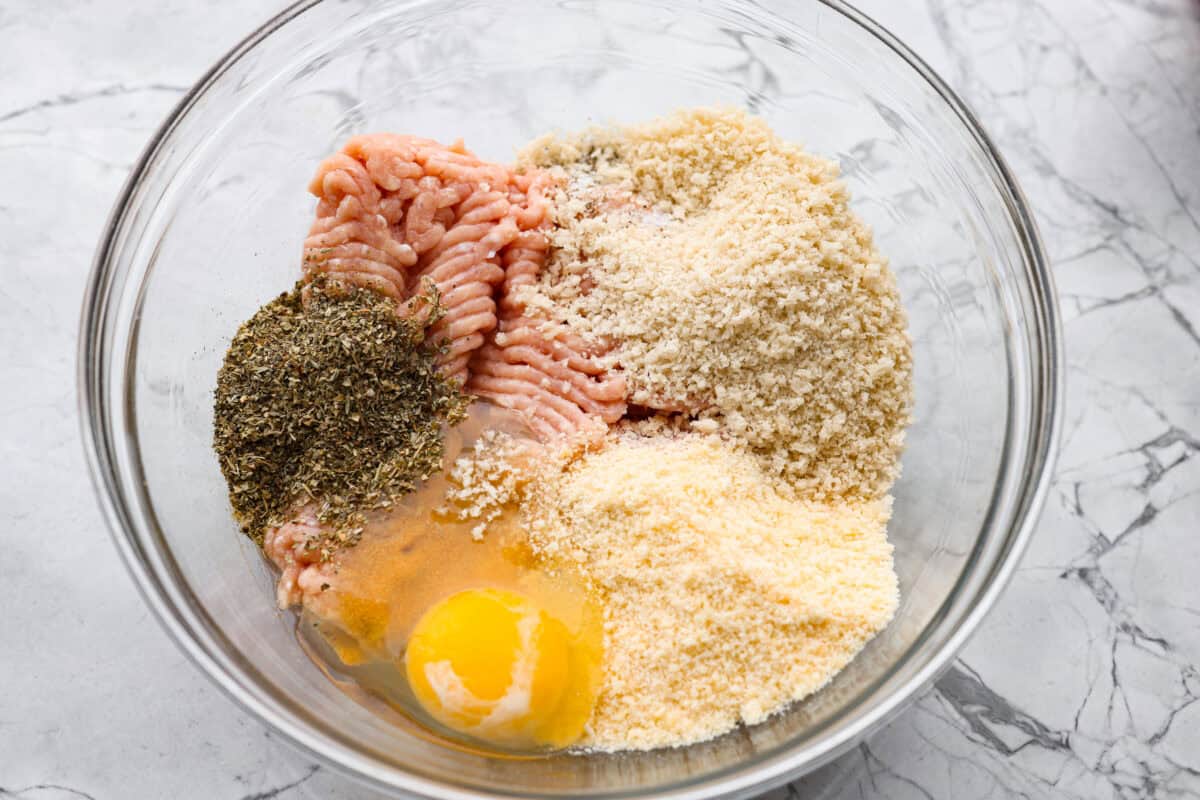 Chicken parmesan meatballs bring all the best parts of chicken parmesan together in one skillet. Think tender chicken meatballs, crispy Parmesan breadcrumbs, saucy marinara, and lots of melted mozzarella. Ground chicken, seasonings, egg, panko breadcrumbs, and parmesan cheese all added to a mixing bowl.