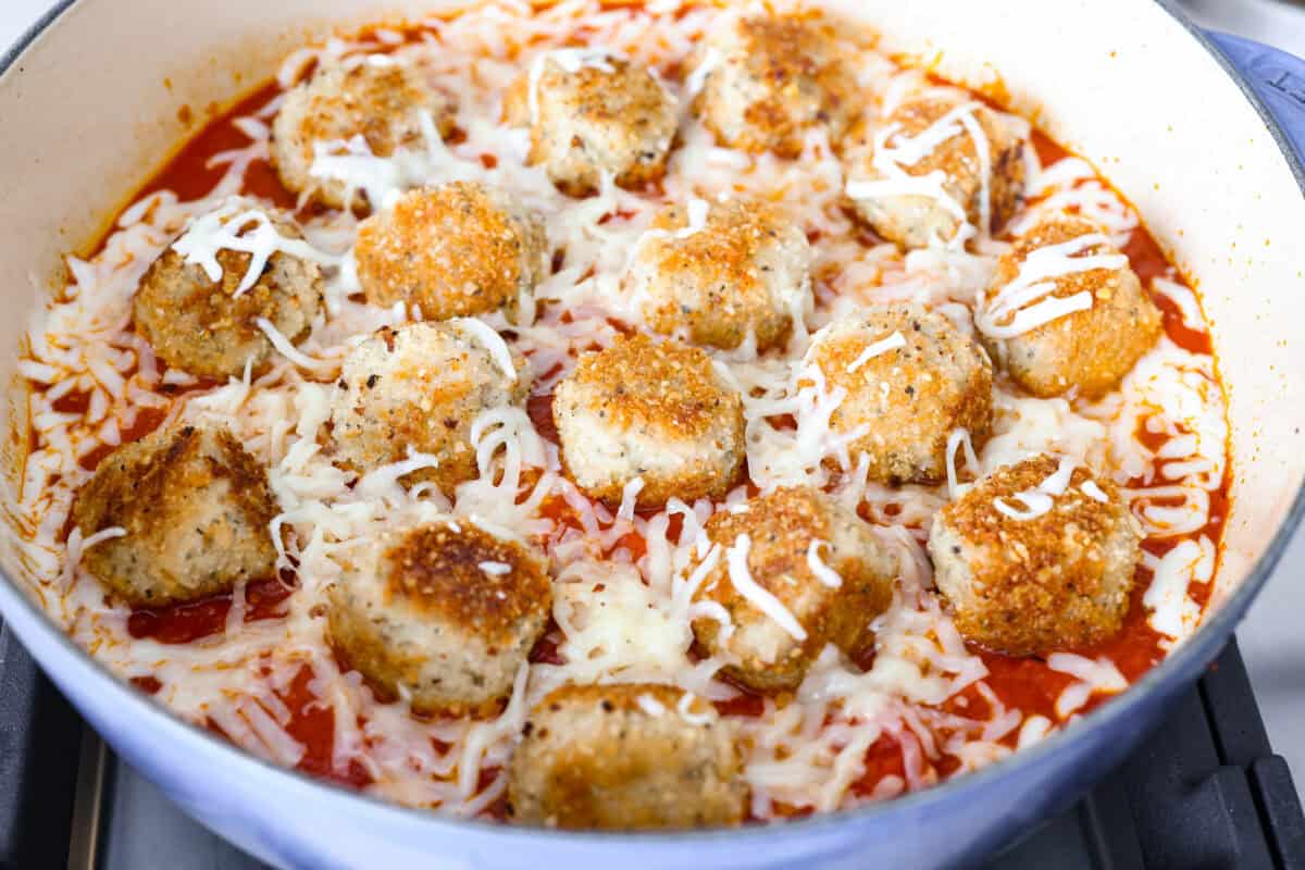 Chicken parmesan meatballs bring all the best parts of chicken parmesan together in one skillet. Think tender chicken meatballs, crispy Parmesan breadcrumbs, saucy marinara, and lots of melted mozzarella. Browned meatballs, marinara sauce and cheese added to the skillet ready to be baked in the oven.