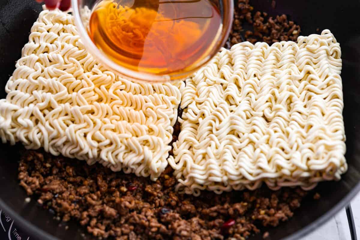 Chili crisp beef ramen noodles are an easy, one-pan dinner you can have on the table in just 20 minutes. Ground beef and ramen noodles cook together in a sweet, savory, and slightly spicy sauce for a quick, filling, and flavorful meal. Ramen noodles placed on top of the ground beef and then beef broth being added to steam the noodles.