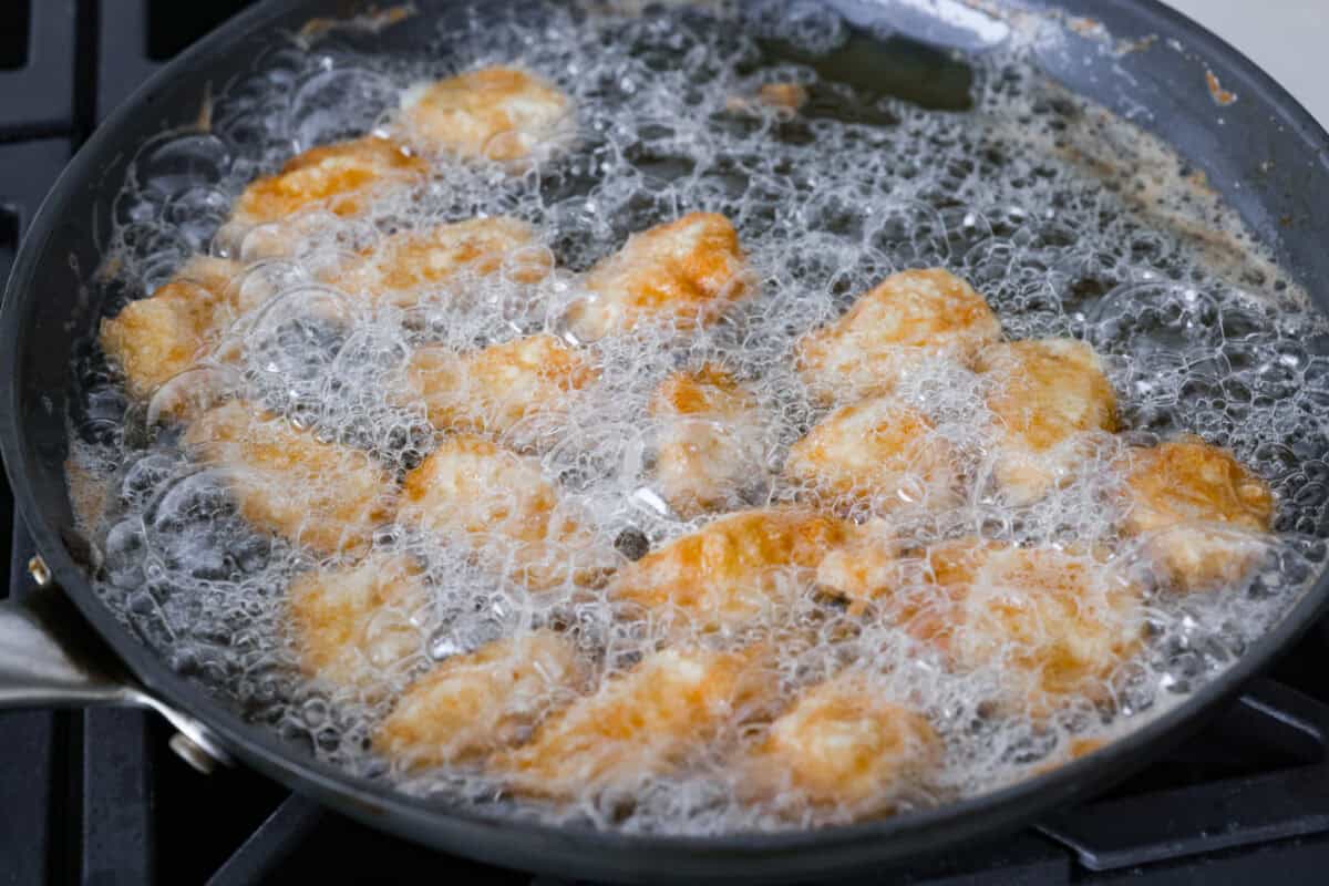 Chinese lemon chicken is lightly fried until golden, then baked in the sticky homemade sauce packed with bright lemon flavor. Make a full take-out-style meal at home with my easy fried rice, cream cheese wontons, and chow mein! Coated chicken pieces frying in oil in a skillet.