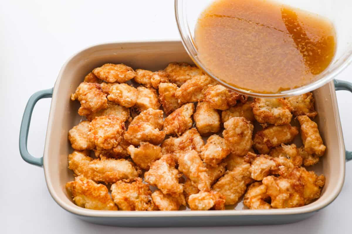 Chinese lemon chicken is lightly fried until golden, then baked in the sticky homemade sauce packed with bright lemon flavor. Make a full take-out-style meal at home with my easy fried rice, cream cheese wontons, and chow mein! Someone pouring the lemon sauce over the browned fried chicken pieces in a 9x13 pan.