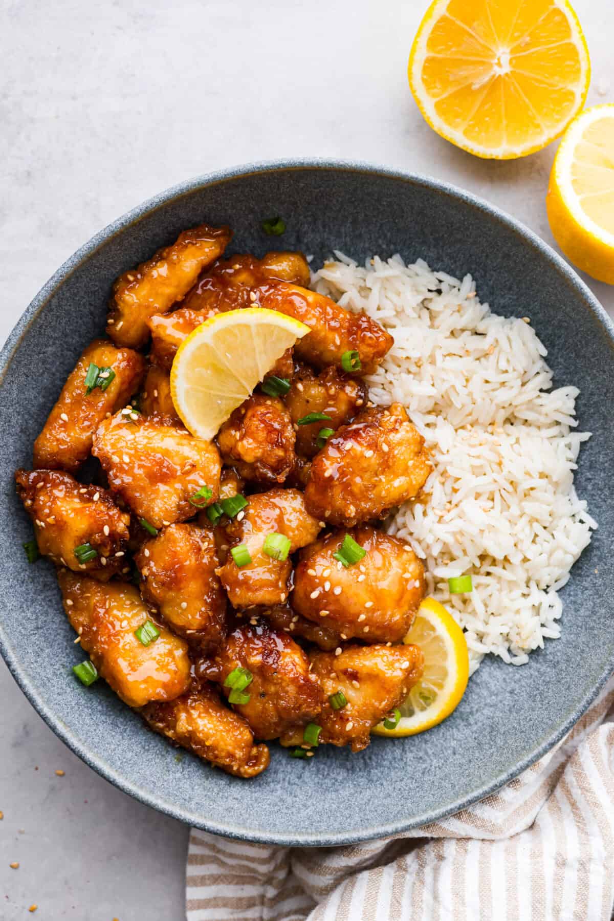 Chinese lemon chicken is lightly fried until golden, then baked in the sticky homemade sauce packed with bright lemon flavor. Make a full take-out-style meal at home with my easy fried rice, cream cheese wontons, and chow mein! Plate of Chinese lemon chicken on a bed of rice.