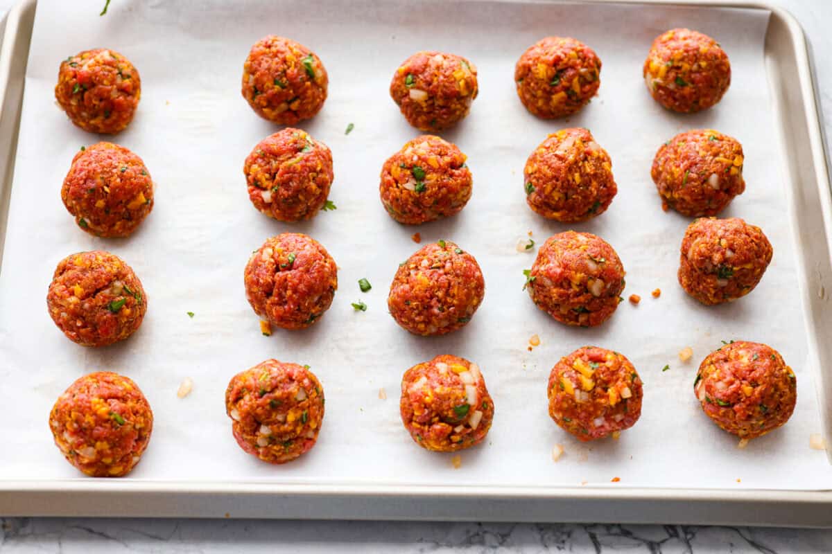 Cowboy meatballs bring big, bold flavors to a classic dinner favorite! Packed with cheesy goodness and spices, they’re simmered in a smoky BBQ sauce with crispy bacon and a little kick from Rotel. So delicious you’ll want to scoop up every last drop. Scooped and shaped meatballs on a parchment lined baking sheet.