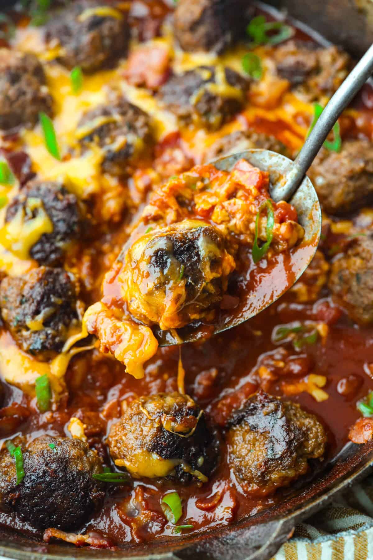 Cowboy meatballs bring big, bold flavors to a classic dinner favorite! Packed with cheesy goodness and spices, they’re simmered in a smoky BBQ sauce with crispy bacon and a little kick from Rotel. So delicious you’ll want to scoop up every last drop. Close up shot of a spoon with a cowboy meatball and the cheesy sauce.