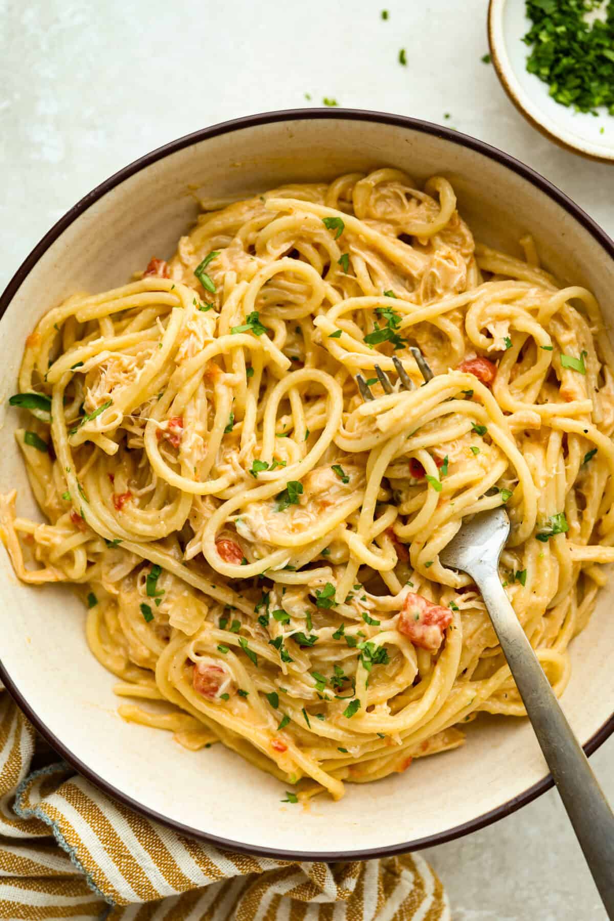 This crockpot chicken spaghetti will have everyone running to the dinner table! The slow cooker does the work while the chicken becomes tender and flavorful, then it's tossed with spaghetti, melty cheese, and a creamy sauce. Bowl with a serving of crockpot chicken spaghetti.