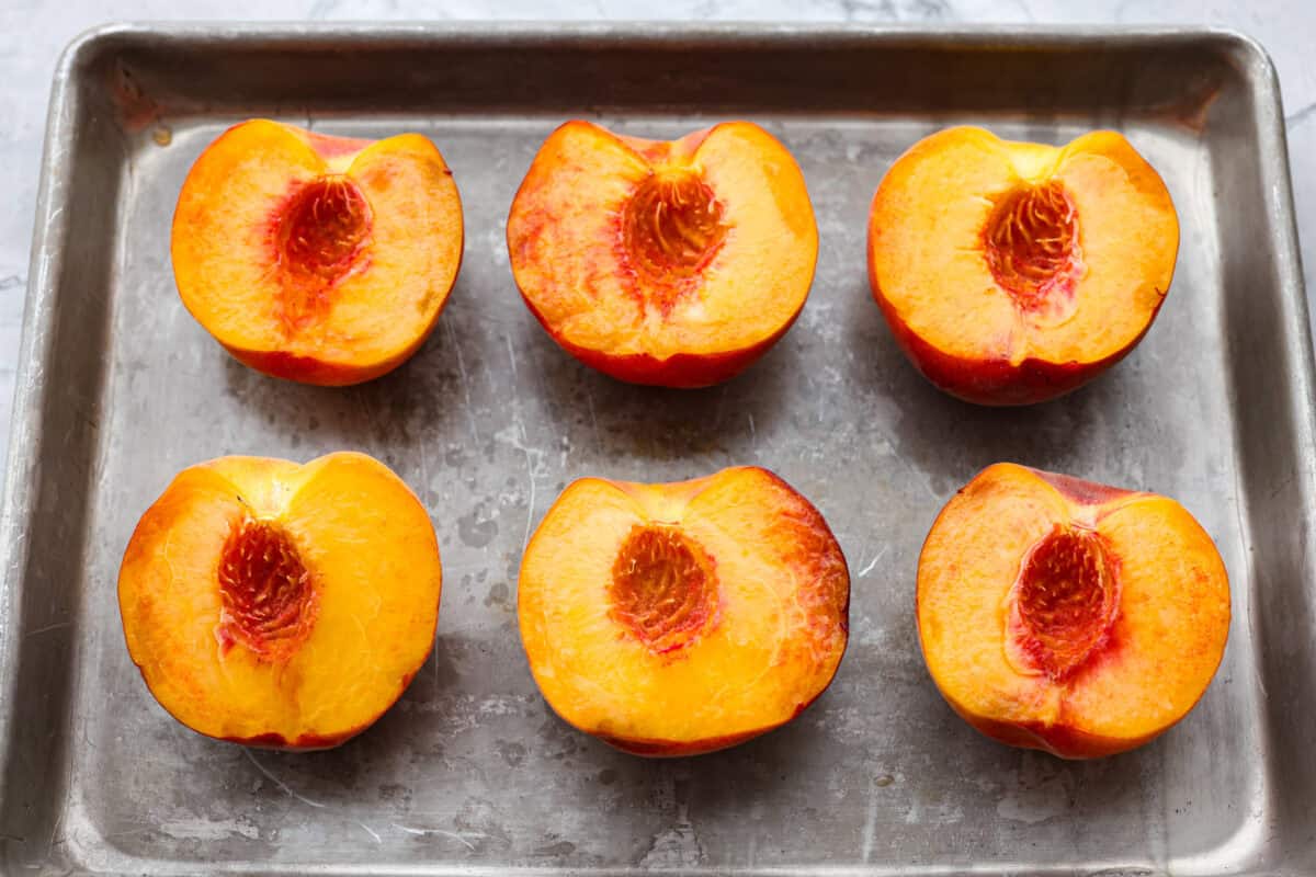 Grilled peaches are one of my favorite ways to turn ripe summer fruit into an easy dessert. The grill brings out their natural sweetness and adds just a little smoky flavor. Serve them warm with vanilla ice cream for a simple treat that feels extra special. Peaches cut in half, pits taken out, and lined up on a baking sheet.