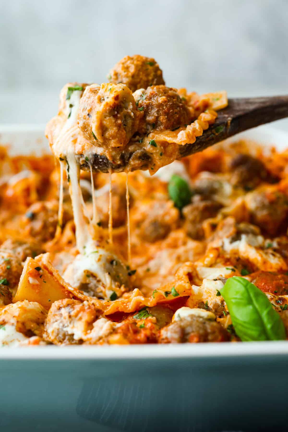Want lasagna but absolutely cannot deal with all that layering tonight? Let me help you. This lazy meatball lasagna is cheesy, cozy, ridiculously easy, and exactly the kind of dinner we need on a busy night. Someone lifting up a large spoonful of lazy meatball lasagna with cheese stretching in between.