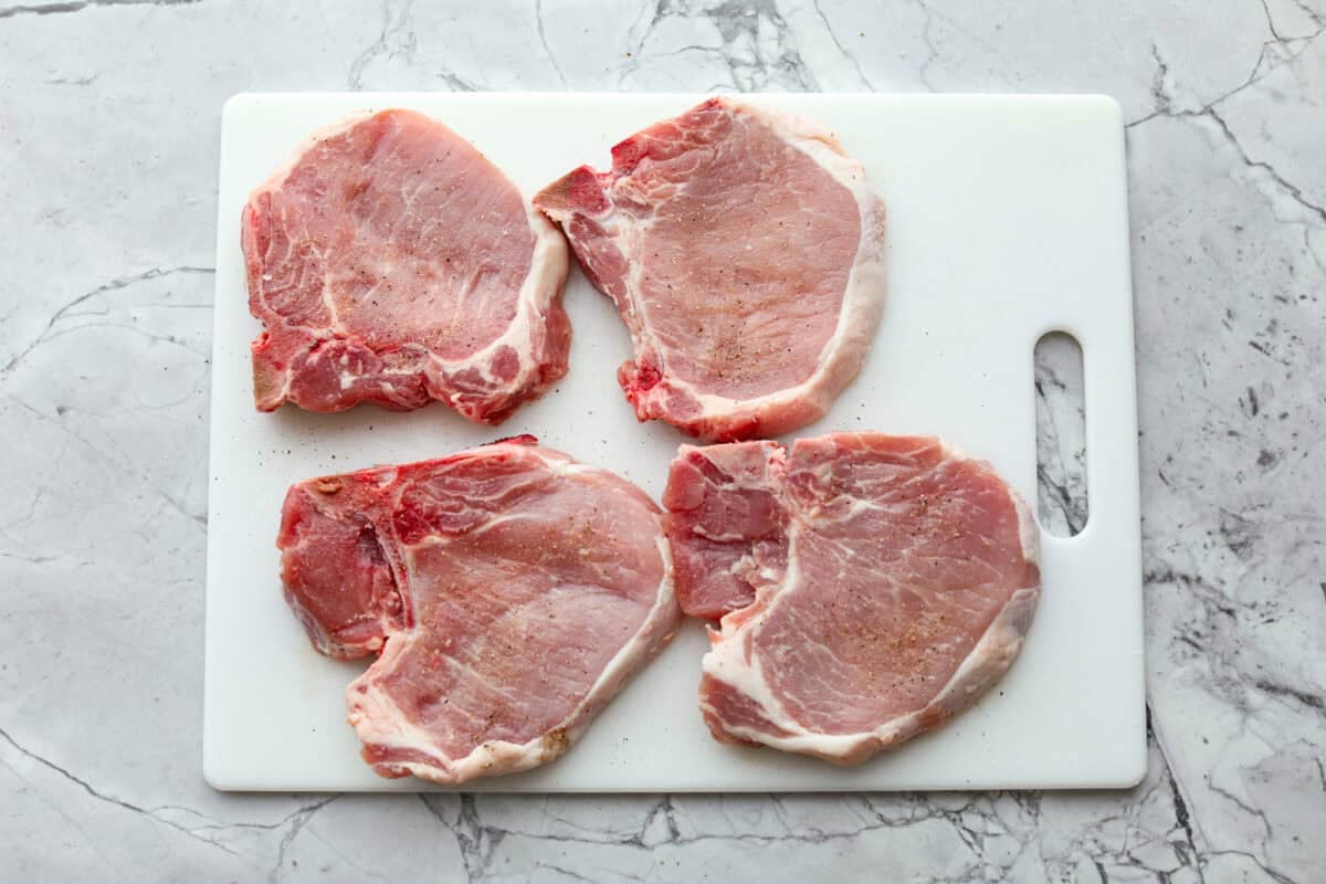Marry Me pork chops are the kind of dinner that earns its name! Tender pork chops are simmered in a rich, creamy Parmesan sauce with garlic, Italian herbs, and sweet, tangy sun-dried tomatoes. One bite and you’ll get why they’re worth proposing over. Pork chops seasoned on a cutting board.