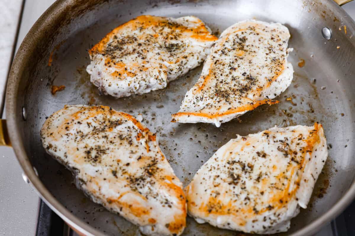 Creamy pepperoncini chicken is an easy one-skillet dinner packed with flavor! Tender chicken is smothered in a rich Parmesan cream sauce with bell peppers and tangy pepperoncini. It's the perfect balance of creamy, savory, and zesty flavor. Chicken breast cooking in a skillet.