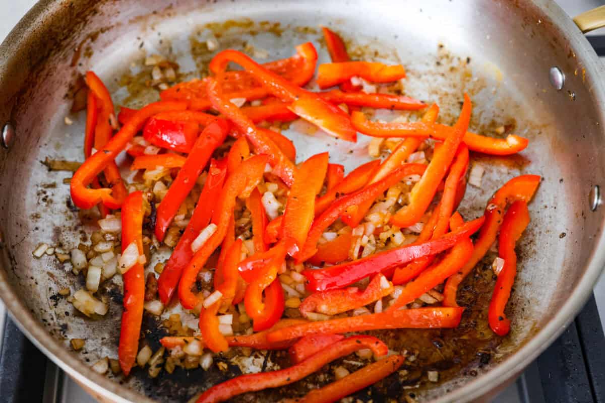 Creamy pepperoncini chicken is an easy one-skillet dinner packed with flavor! Tender chicken is smothered in a rich Parmesan cream sauce with bell peppers and tangy pepperoncini. It's the perfect balance of creamy, savory, and zesty flavor. Peppers and onions cooking in a skillet.