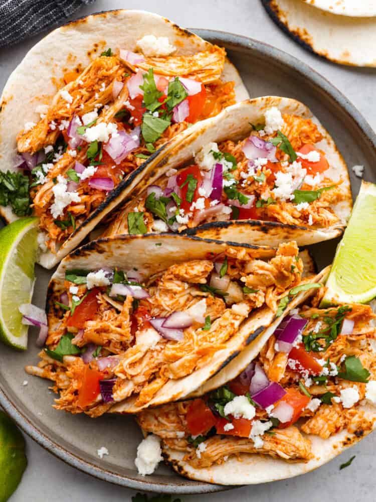 Shredded chicken tacos turn cooked chicken into juicy, flavorful tacos with salsa, lime, and a few simple seasonings. Use rotisserie chicken or choose from four easy ways to cook and shred your own. Shredded chicken tacos on a black plate with limes next to them.