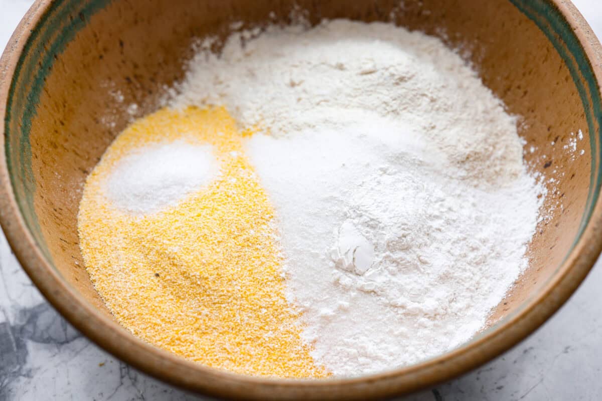Butter swim cornbread bakes in a whole stick of butter, giving it crisp, golden edges and a soft, tender center. My secret ingredient is a can of creamed corn, which makes it extra moist and adds even more sweet corn flavor. Dry ingredients added to a bowl