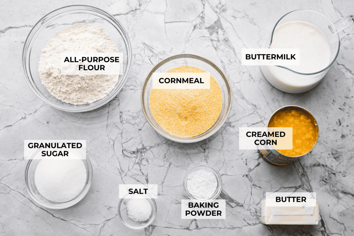 Butter swim cornbread bakes in a whole stick of butter, giving it crisp, golden edges and a soft, tender center. My secret ingredient is a can of creamed corn, which makes it extra moist and adds even more sweet corn flavor. overhead shot of labeled butter sim cornbread ingredients.