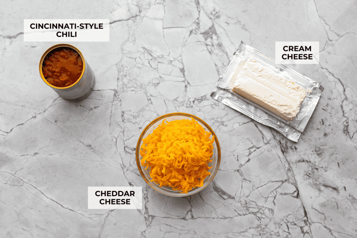 Cincinnati chili dip is the easiest game day appetizer you didn’t know you needed! Also called Skyline dip, it has just three ingredients: cream cheese, Cincinnati-style chili, and melty cheddar cheese. Overhead shot of labeled Cincinnati chili dip ingredients.
