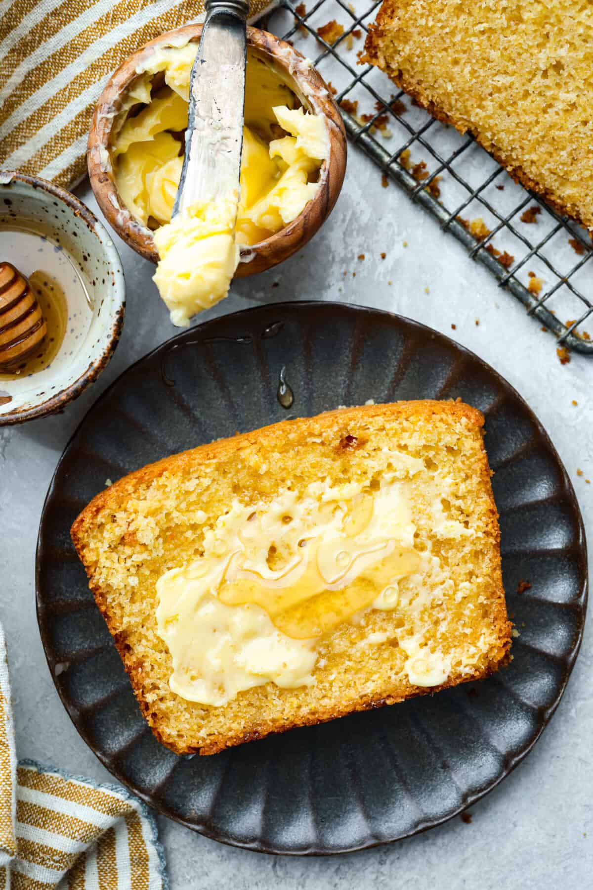 This cornbread loaf is soft, buttery, and just sweet enough, with crisp golden edges and a tender crumb. Baking it in a loaf pan gives classic cornbread a fun twist that’s easy to slice and serve with chili, stew, or your favorite comfort food. Plated slice of cornbread spread with butter and honey.