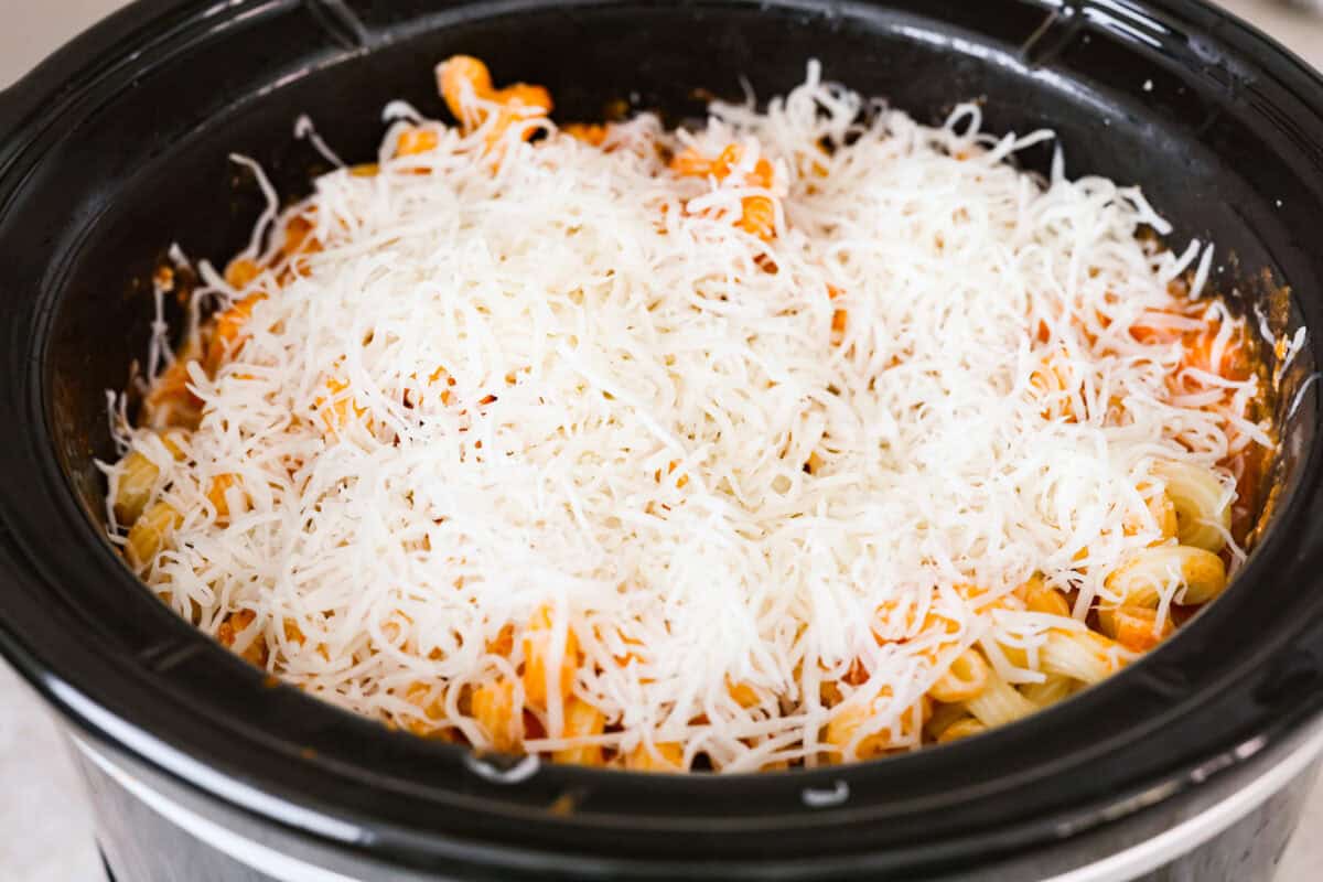 Crockpot creamy chicken pasta is the kind of dinner I need on a busy weeknight! Tender chicken cooks all day in a creamy marinara sauce, then you stir in pasta and cheese for the easiest comfort food dinner. Cheese added to the top of the ingredients in the crockpot.