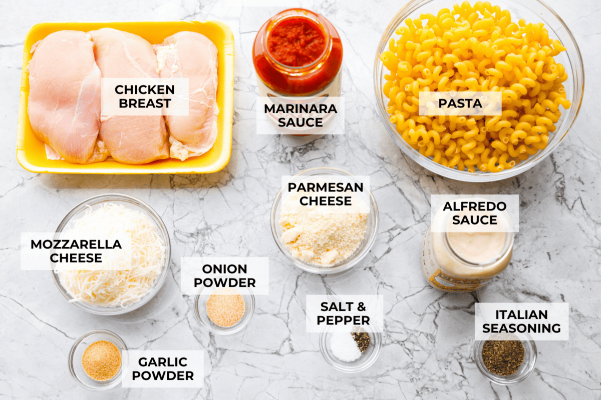 Crockpot creamy chicken pasta is the kind of dinner I need on a busy weeknight! Tender chicken cooks all day in a creamy marinara sauce, then you stir in pasta and cheese for the easiest comfort food dinner. Overhead shot of labeled crockpot creamy chicken pasta ingredients.