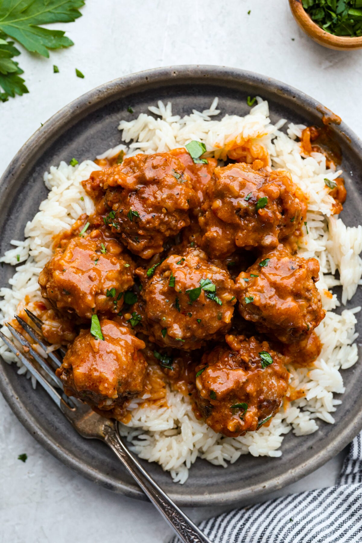 Porcupine Meatballs are juicy, well-seasoned meatballs with tender rice simmered in a rich, tangy tomato sauce. This recipe comes straight from my grandma’s kitchen, and trust me, your family’s about to be obsessed! A plated photo of porcupine balls on some rice with a fork.