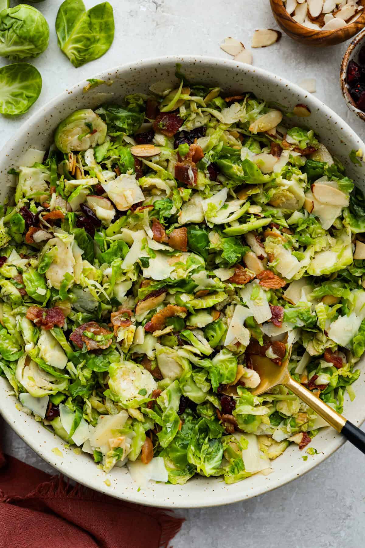 I didn’t always get excited about Brussels sprouts, but this Brussels sprouts salad with bacon changed that. Crispy bacon, tart cranberries, toasted almonds, and Parmesan make every bite so good, with a warm maple-orange dressing to tie it all together. Large bowl of warm Brussels sprouts salad with bacon with a serving spoon.