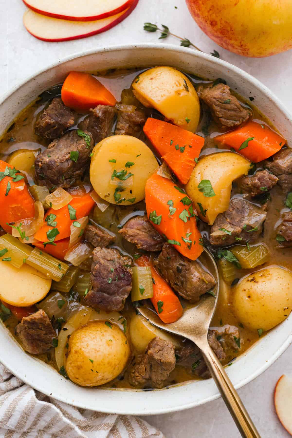 Bowl of apple cider beef stew with a gold spoon. 