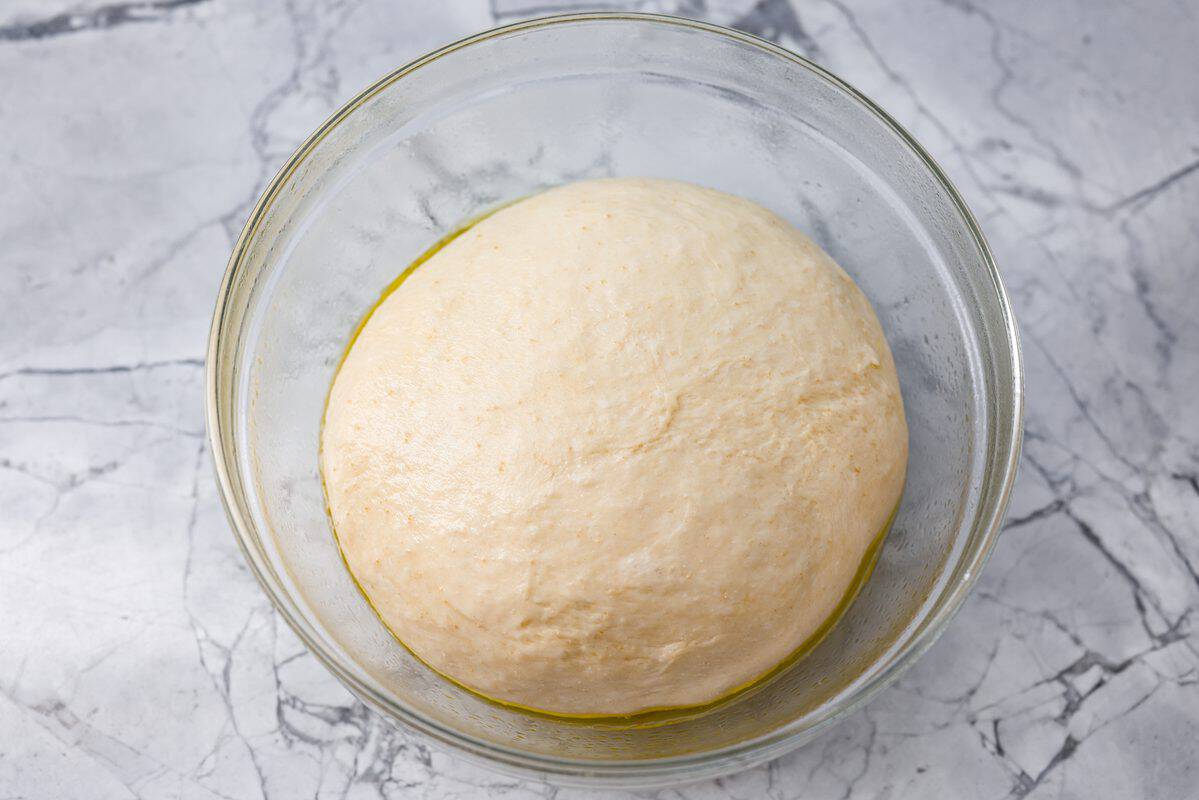 Mound of dough covered in olive oil in a glass bowl ready to raise. 