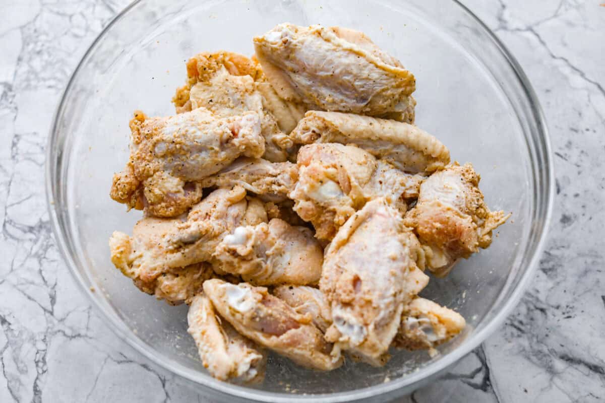 Chicken wings tossed in the bowl and coated in the seasonings. 