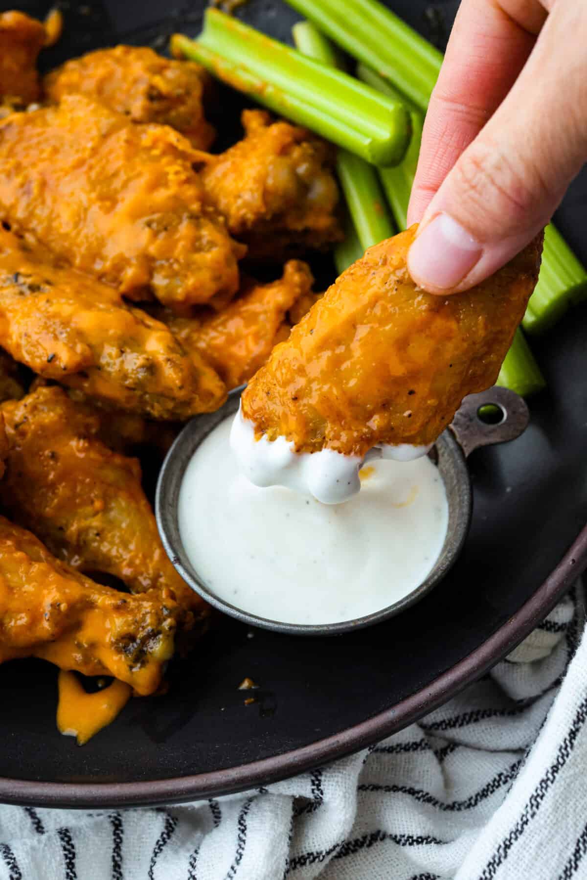 Someone dipping a chicken wing into the ranch dressing. 