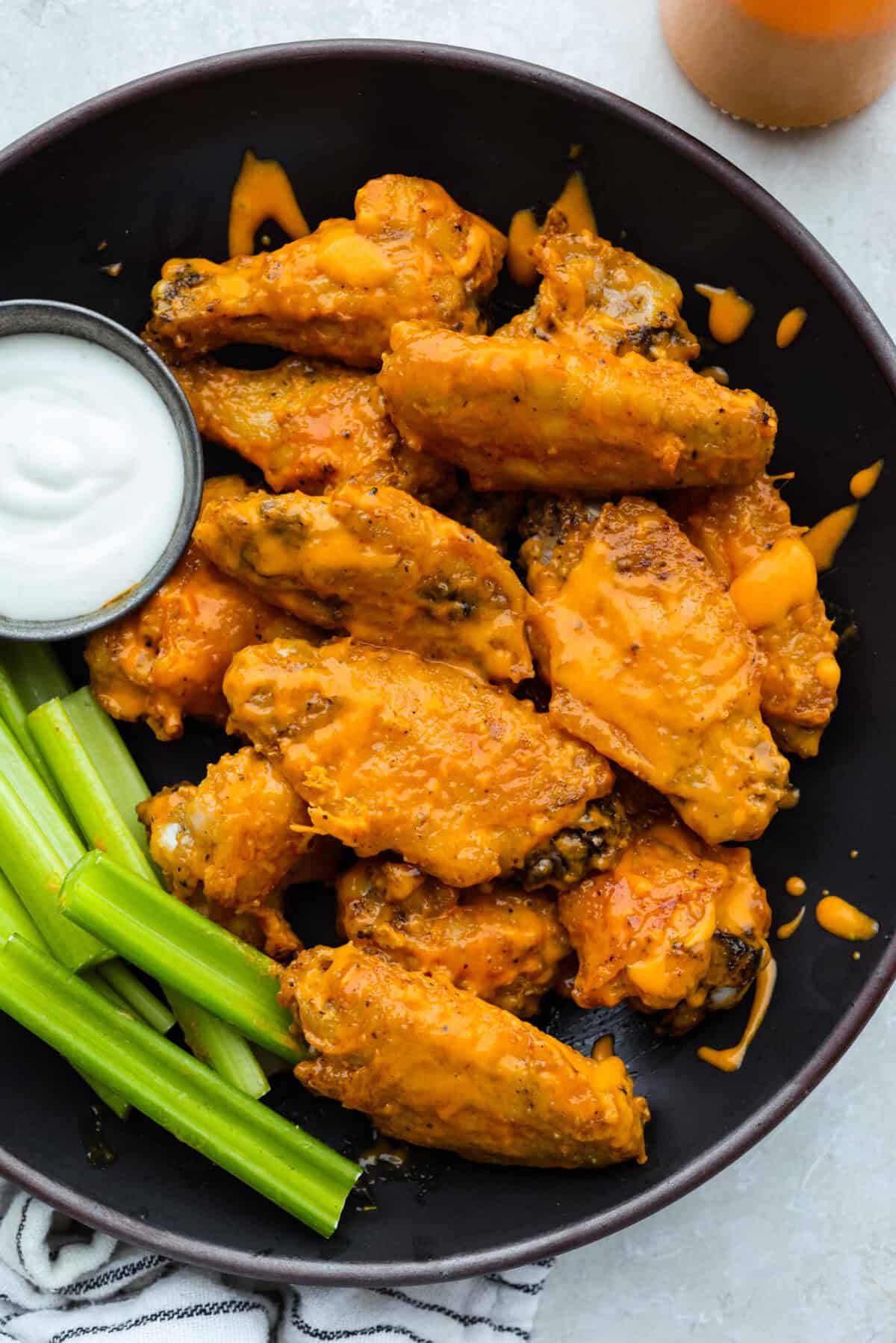 Plate of saucy Gold Fever chicken wings with ranch and celery sticks on the side.