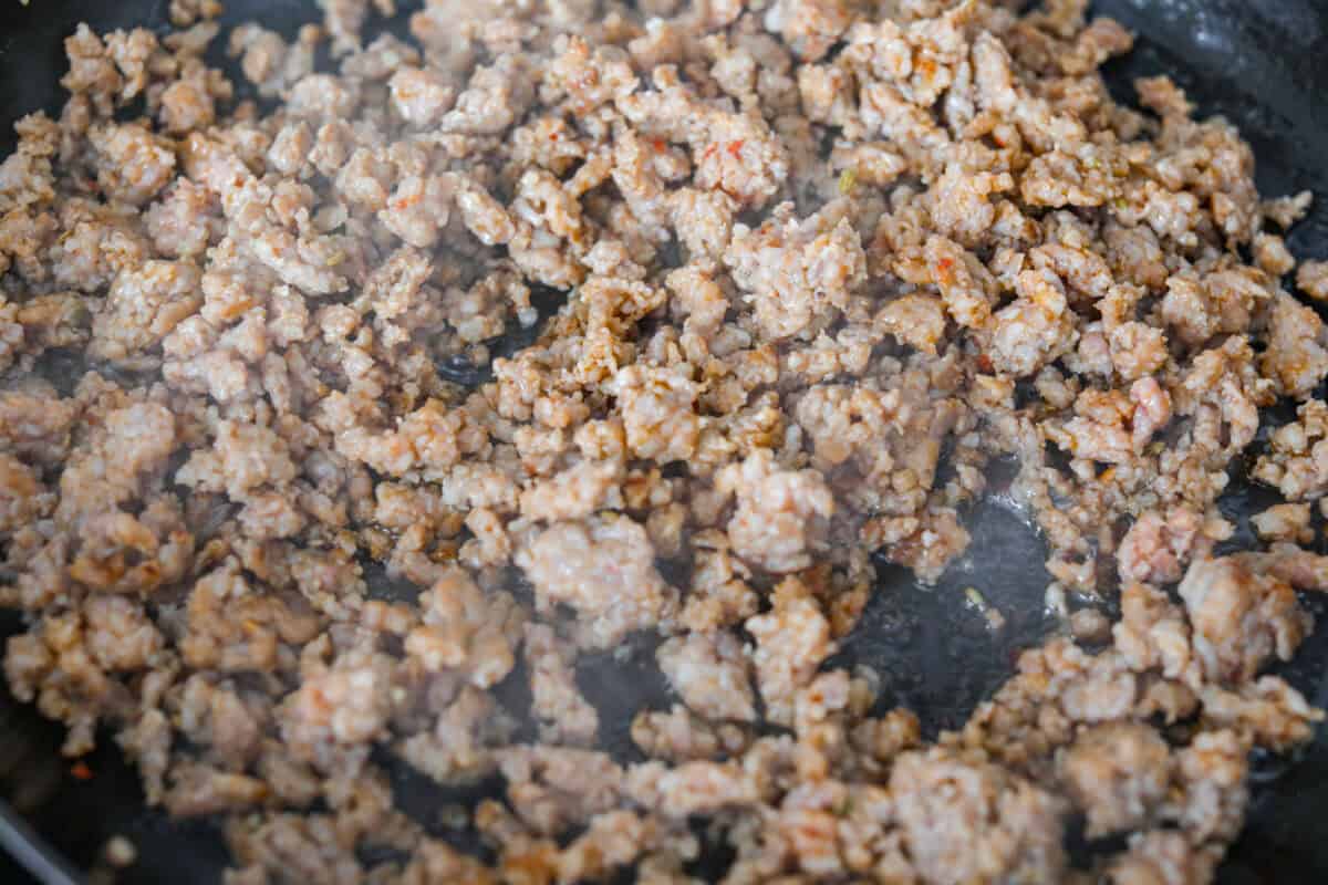 My hot cowboy dip is what I'm bringing to the next game day party! It's loaded with savory sausage, gooey cheese, and a little kick from the jalapeños. Everything comes together in one skillet, so there's less cleanup and more time to dig in! Sausage cooking in a skillet.