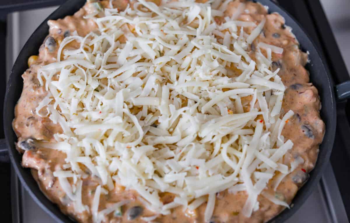 My hot cowboy dip is what I'm bringing to the next game day party! It's loaded with savory sausage, gooey cheese, and a little kick from the jalapeños. Everything comes together in one skillet, so there's less cleanup and more time to dig in! Cheese added to the top of all of the melted and combined ingredients.