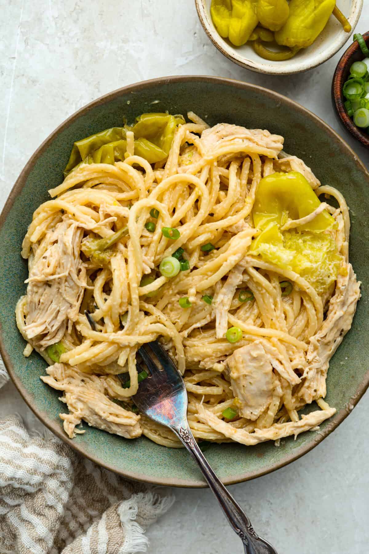 This Mississippi chicken spaghetti gives classic Mississippi chicken a cheesy pasta upgrade! Tender chicken, tangy pepperoncini peppers, ranch, and melty Colby Jack come together with spaghetti for an easy slow cooker dinner packed with flavor. Serving portion of mississippi chicken spaghetti in a bowl with a fork.