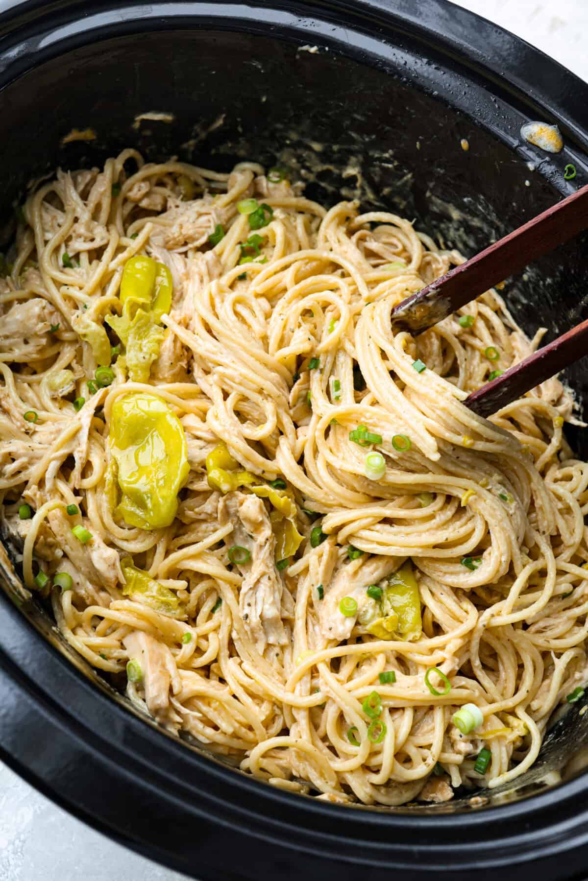 This Mississippi chicken spaghetti gives classic Mississippi chicken a cheesy pasta upgrade! Tender chicken, tangy pepperoncini peppers, ranch, and melty Colby Jack come together with spaghetti for an easy slow cooker dinner packed with flavor. Top down shot of a slow cooker with Mississippi chicken spaghetti all mixed together and ready to serve.