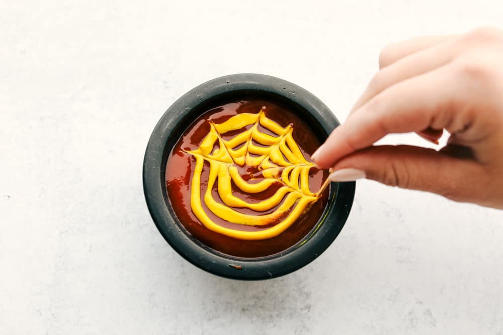 Ketchup and mustard in a bowl with the mustard being shaaped with a toothpick like a spider web.