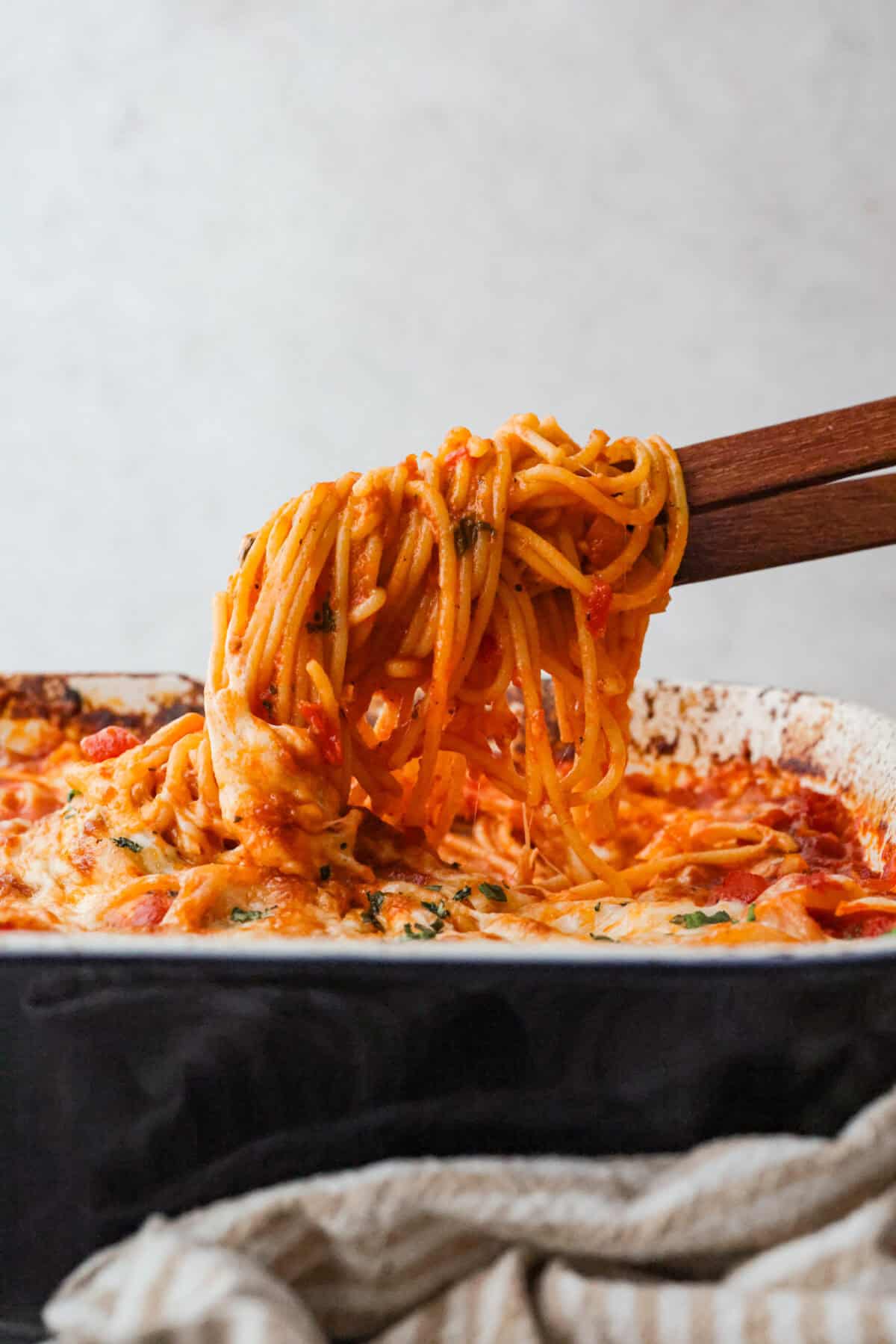 This no boil spaghetti bake makes pasta night SO easy! Everything goes straight into one baking dish, uncooked spaghetti included, then bakes under a layer of melty mozzarella for a cozy, cheesy dinner with hardly any prep. Someone lifting a scoop of the no boil spaghetti bake out of the baking dish.