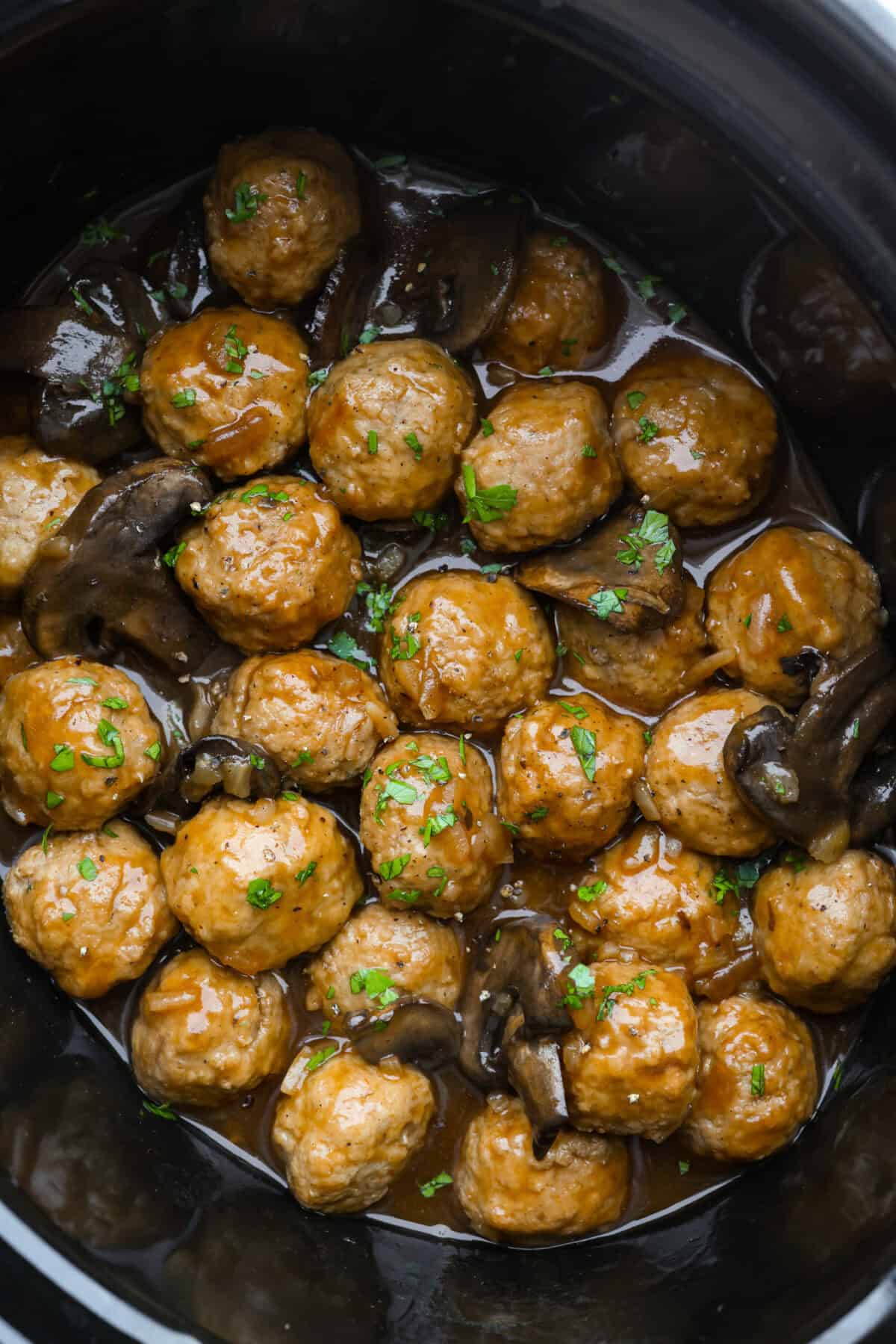 Slow cooker salisbury meatballs in a slow cooker garnished with parsley. 