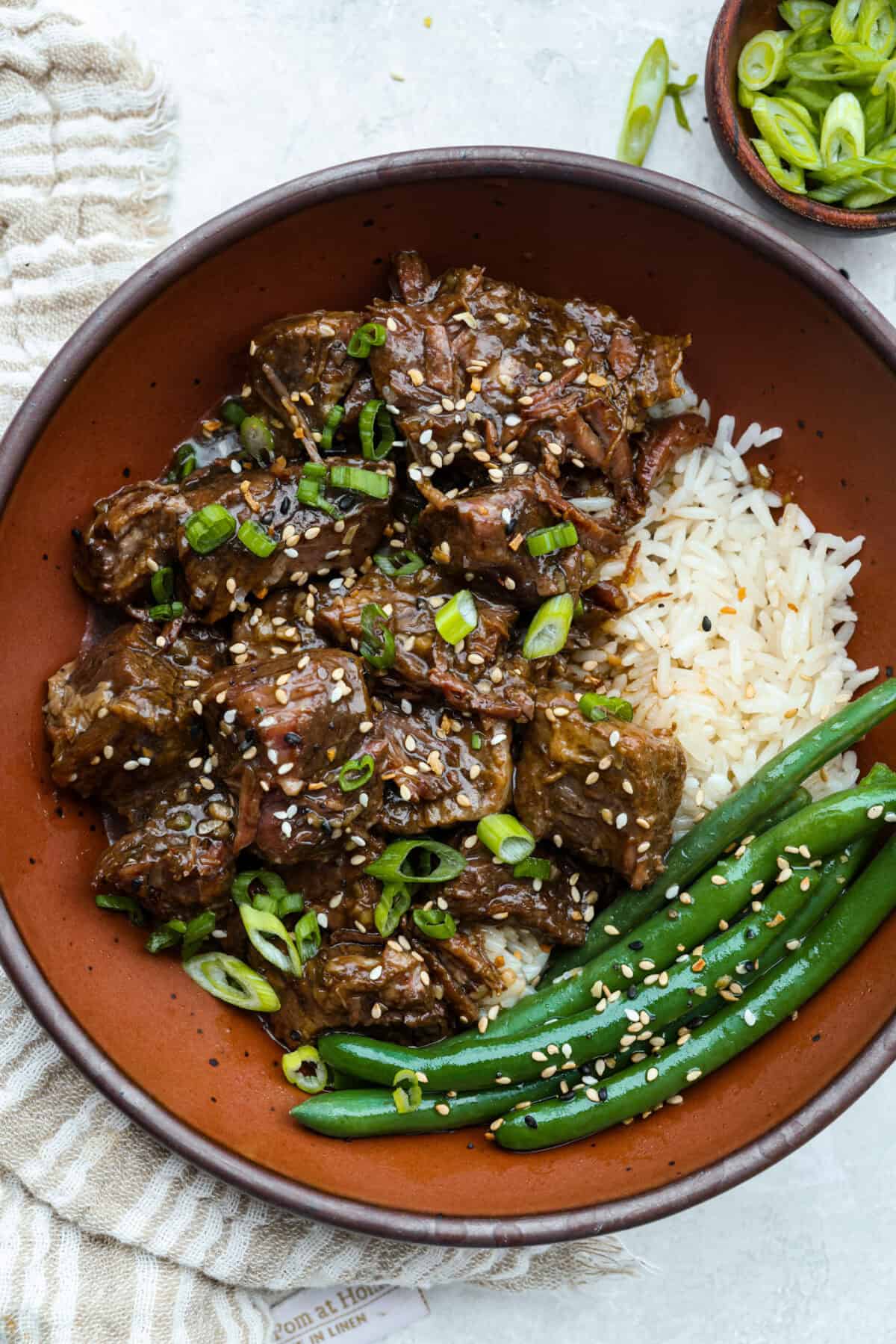 I love a good takeout-inspired dinner, especially when my slow cooker does most of the work! My slow cooker sesame ginger beef is packed with sweet and savory flavor, and the chuck roast cooks until it's perfectly tender. Plated slow cooker sesame ginger beef with rice and green beans.