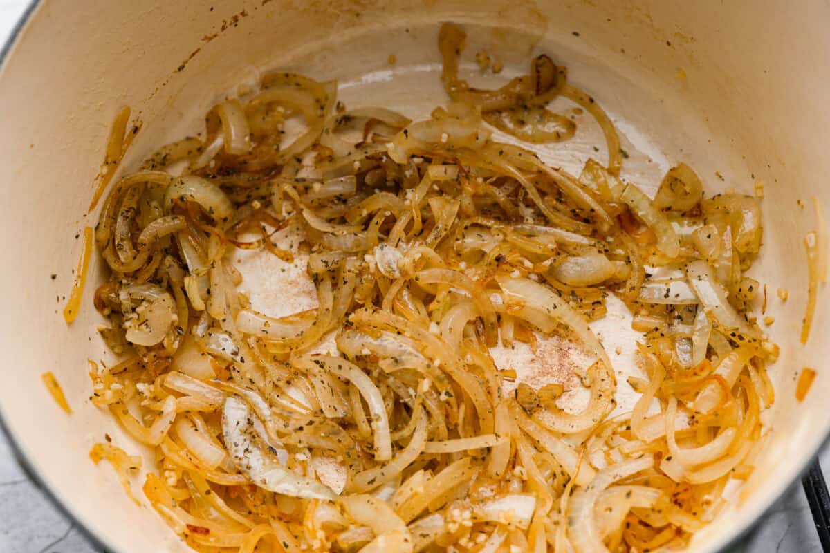 Onions, seasonings and garlic cooking in the bottom of a dutch oven. 