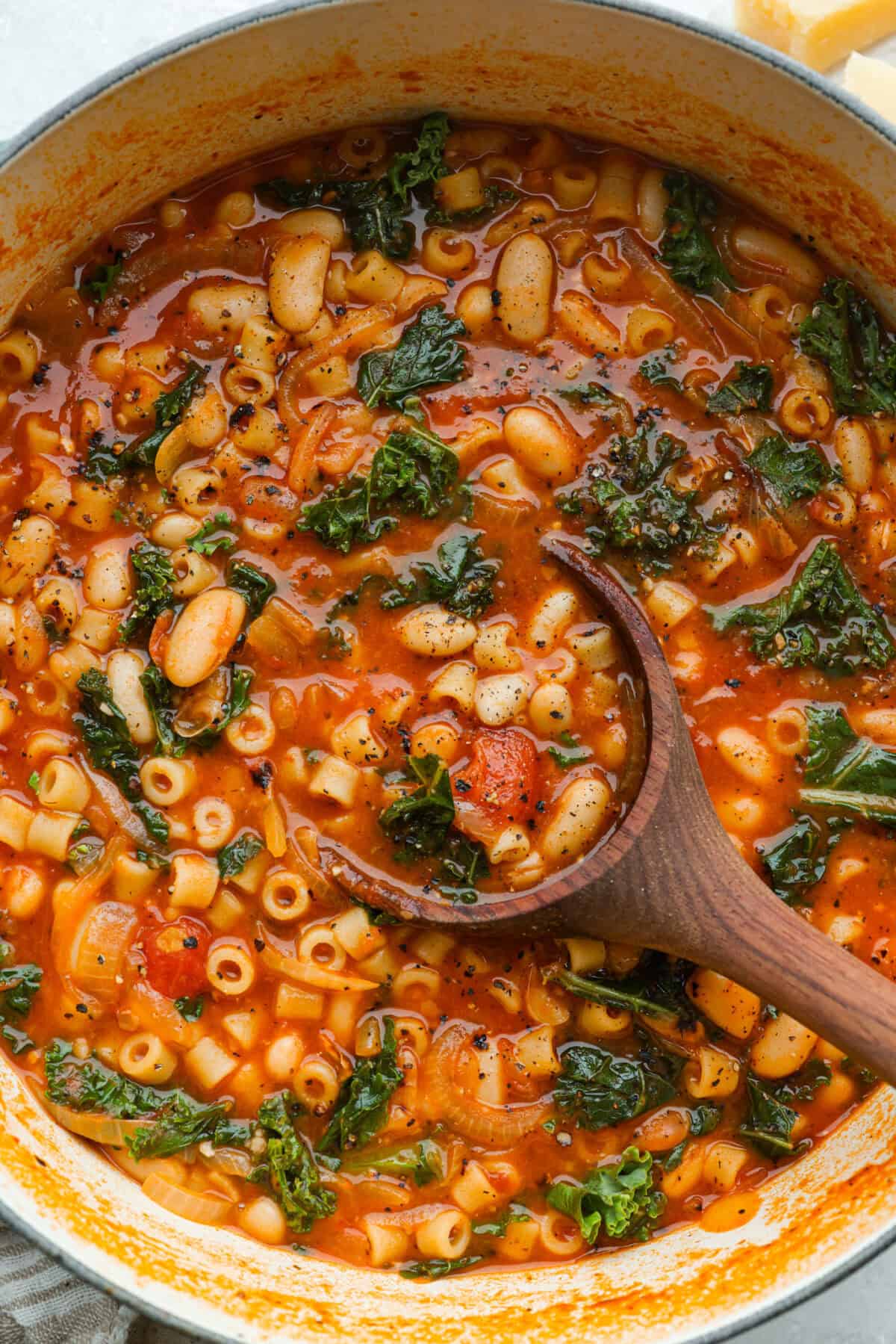 Large dutch oven with cooked Stanley Tucci pasta fagioli soup and a wooden ladle.