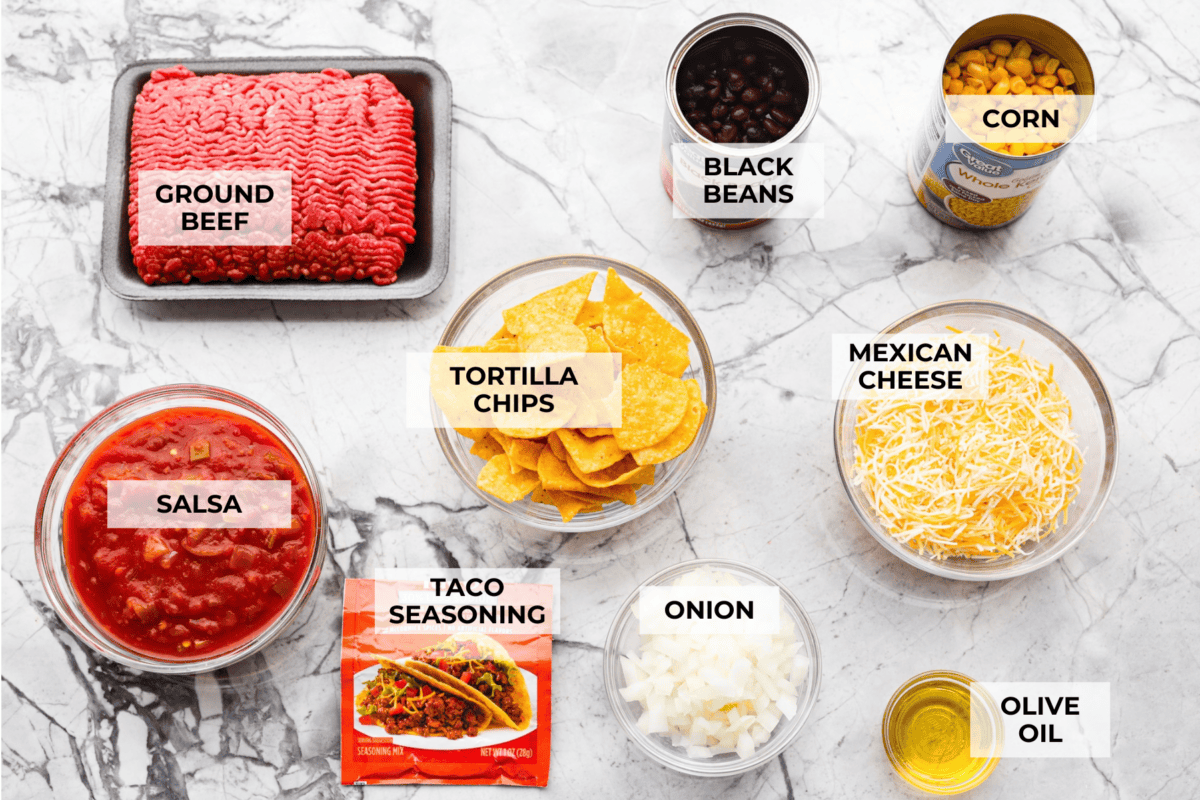 My taco casserole has everything you love about tacos baked into one cheesy, hearty dinner! It's loaded with seasoned ground beef, beans, corn, salsa, and tortilla chips. I love topping mine with sour cream, avocado, and fresh cilantro! Overhead shot of labeled taco casserole ingredients.